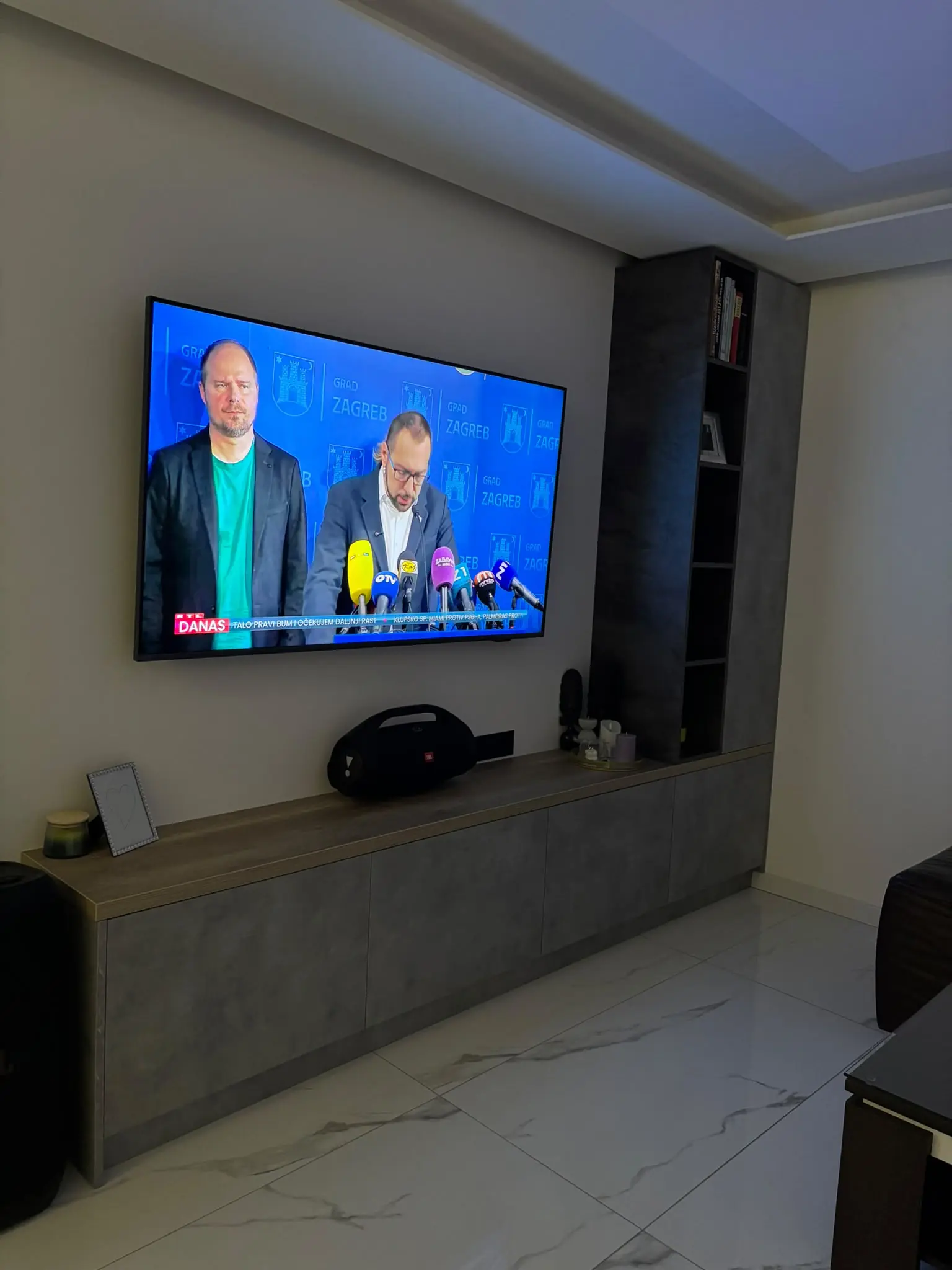 Dnevni boravak s visećim televizorom i dugom sivom komodom uz zid